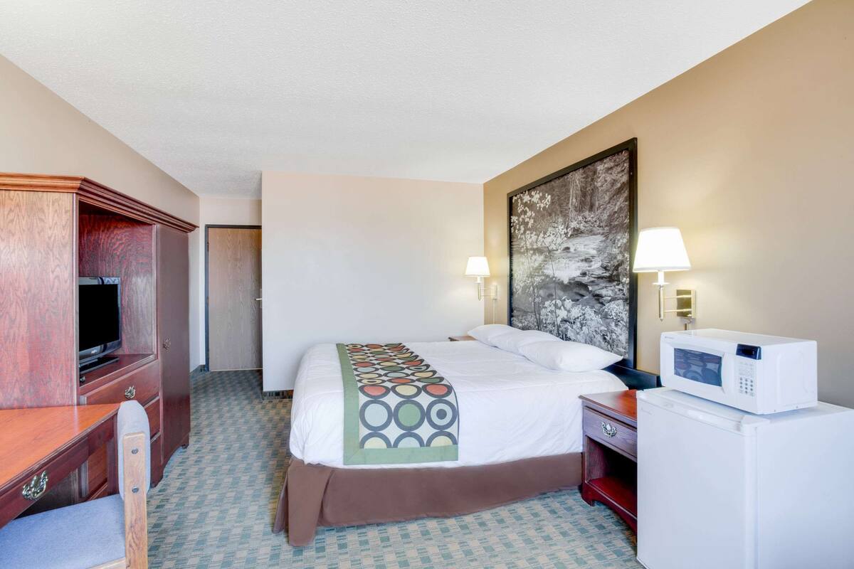 A hotel room with a bed, a TV, a microwave, a desk, and a chair.