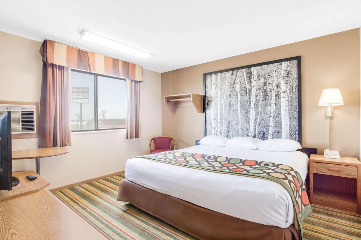 A hotel room with a bed, a TV, a desk, a chair, a lamp, and a window with curtains.