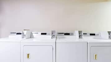A row of white laundry machines with control panels, arranged in a row against a plain wall.