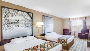 A hotel room with two beds, a large window with curtains, a small table, and two purple armchairs.