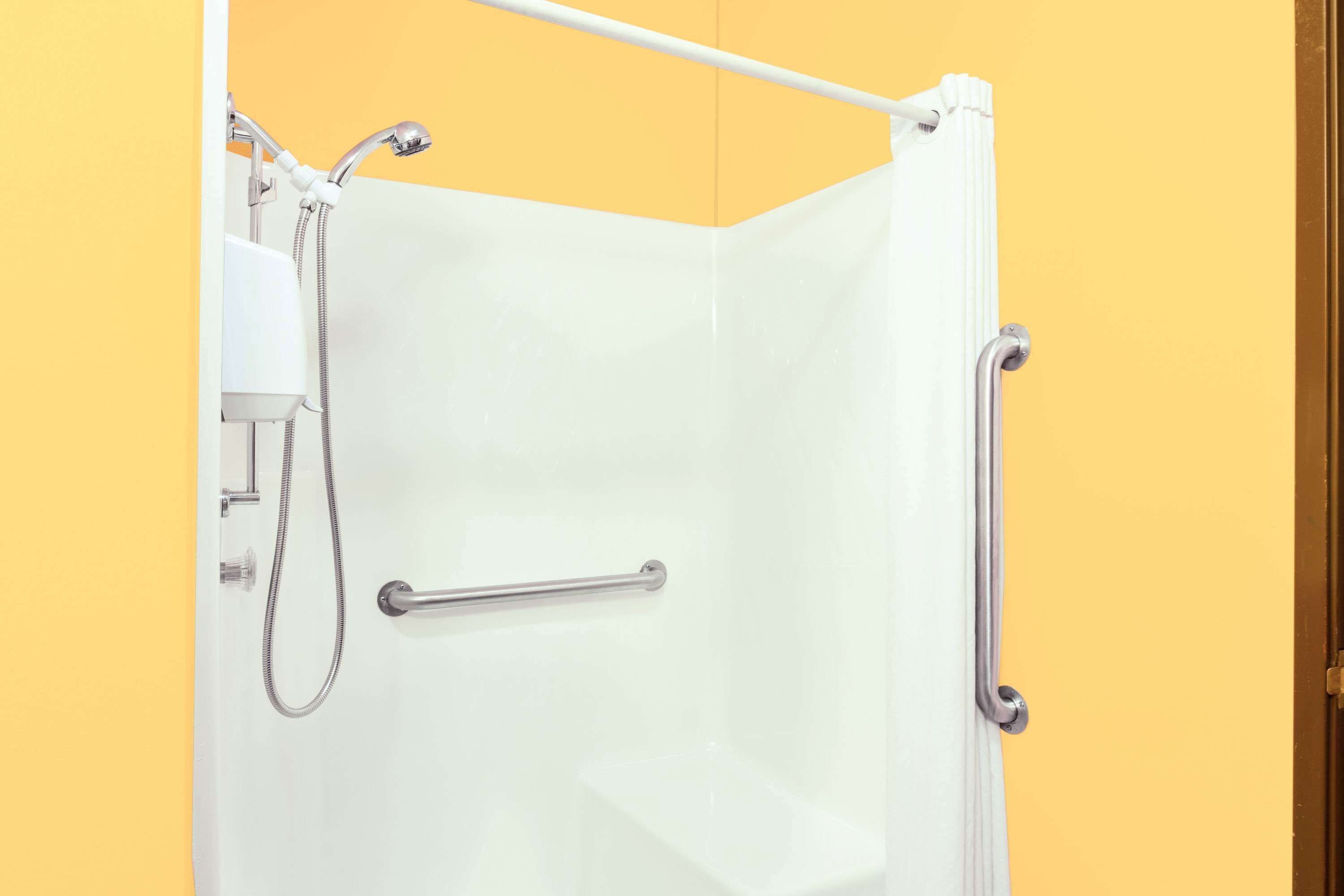 Doccia con soffione estraibile, barra di sostegno e vasca da bagno bianca.