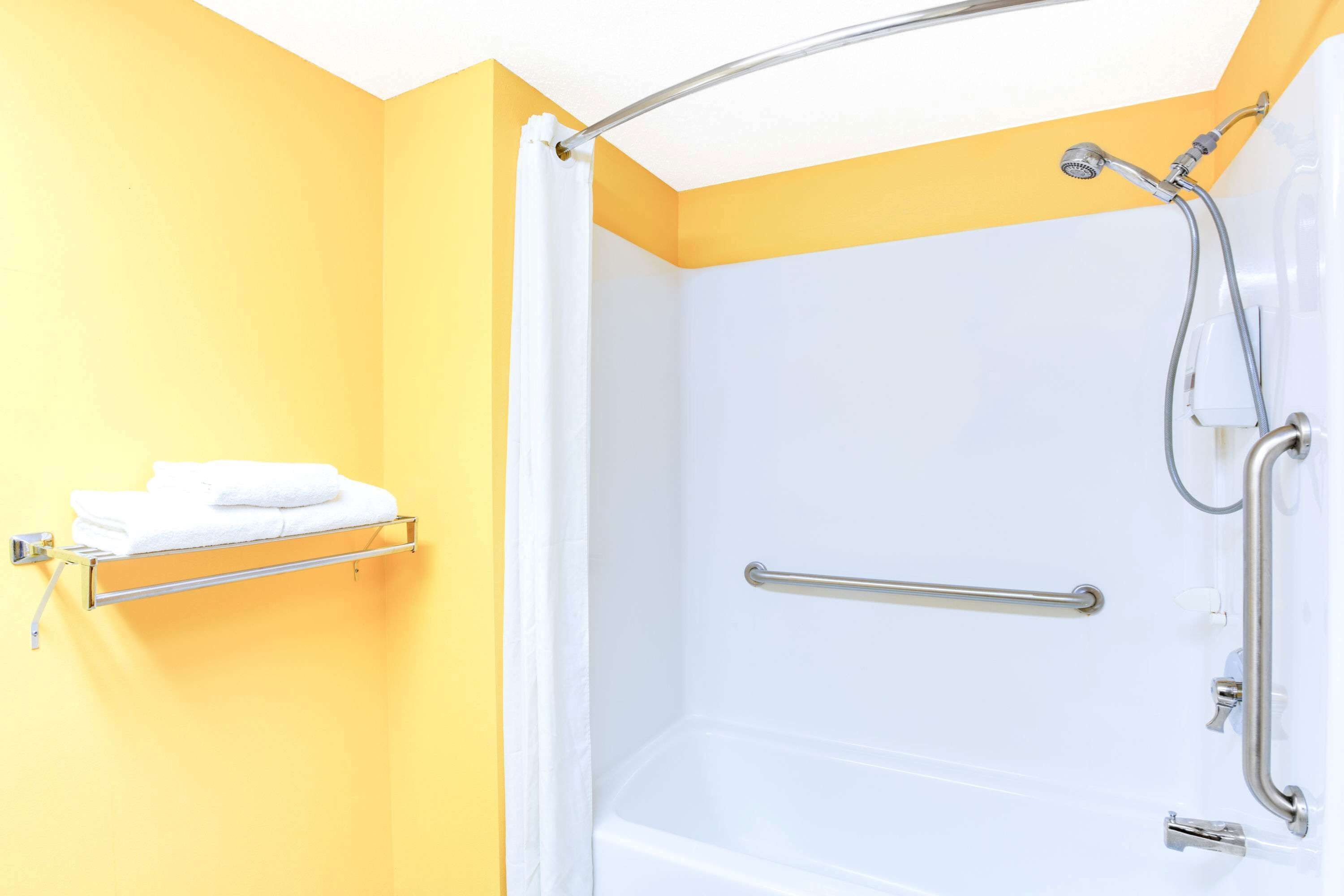 A bathroom with a white bathtub, a shower with a handheld showerhead, a grab bar, and a towel rack with a folded towel.