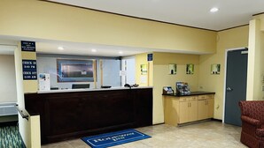 A hotel reception area with a check-in counter, a blue mat with the hotel name, a non-smoking sign, and a clock indicating check-in and check-out times.