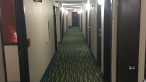 A hotel hallway with carpeted floors, doors on both sides, and an exit sign above.
