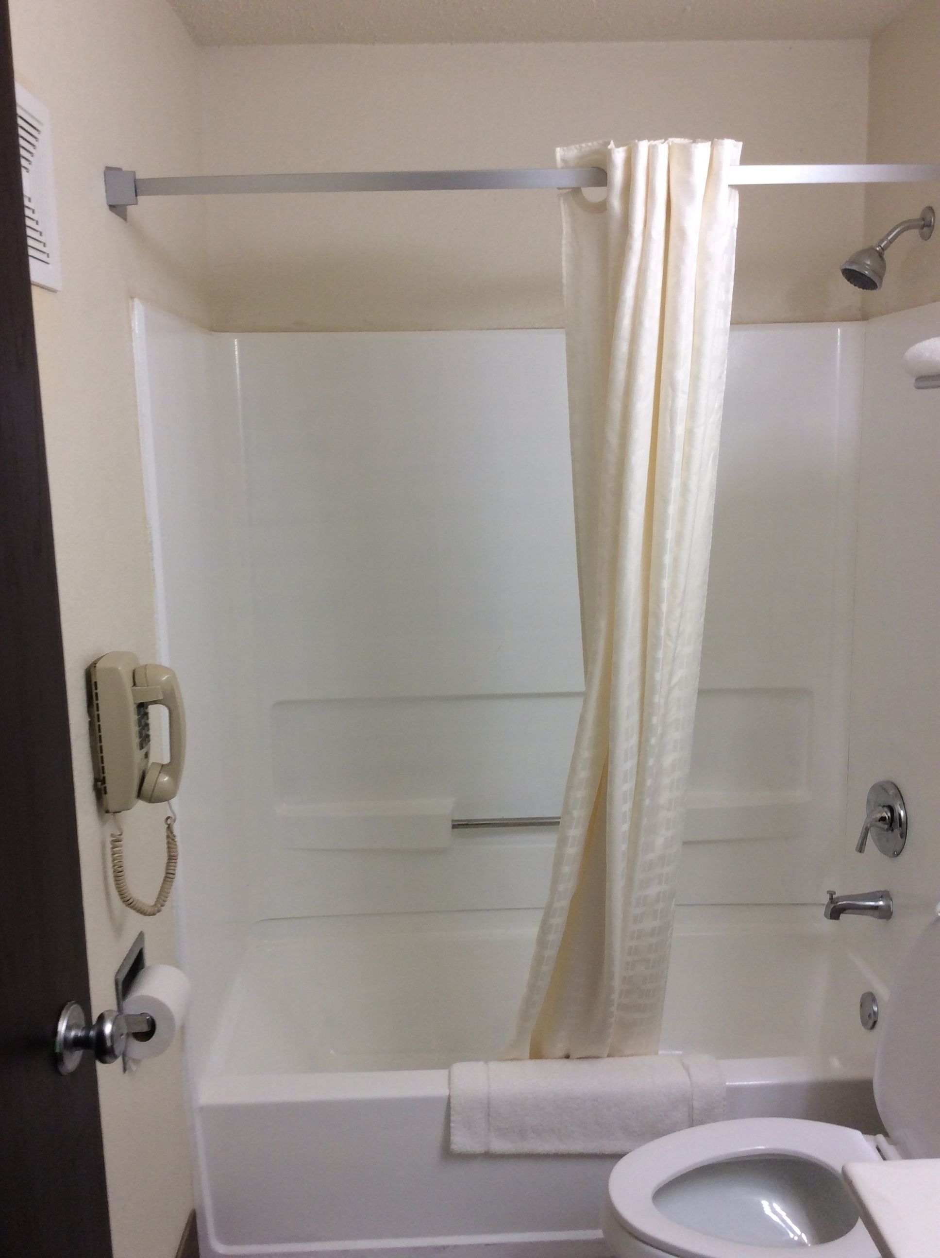 A bathroom with a bathtub, toilet, and a telephone mounted on the wall.