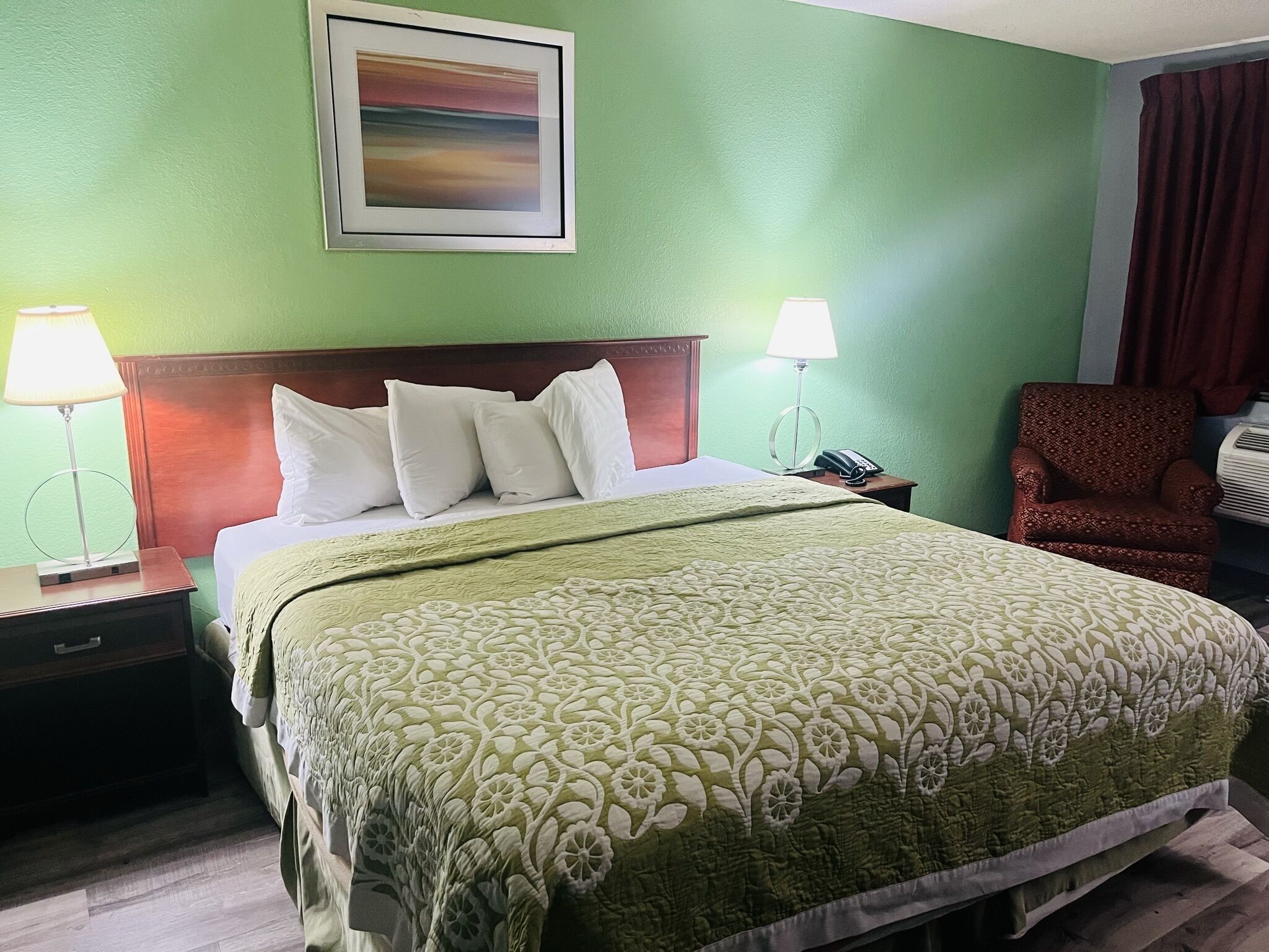 A hotel room with a bed, two bedside lamps, a chair, a framed picture on the wall, and a telephone on the nightstand.