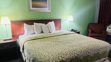 A hotel room with a bed, two bedside lamps, a chair, a framed picture on the wall, and a telephone on the nightstand.