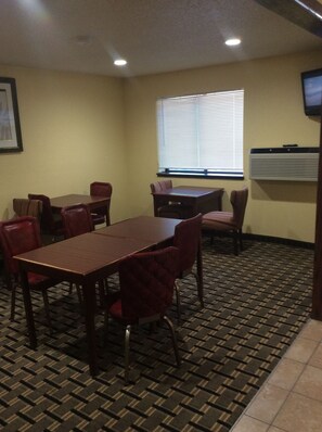 A conference room with a rectangular table and six chairs, a window with blinds, a framed picture on the wall, and an air conditioning unit.