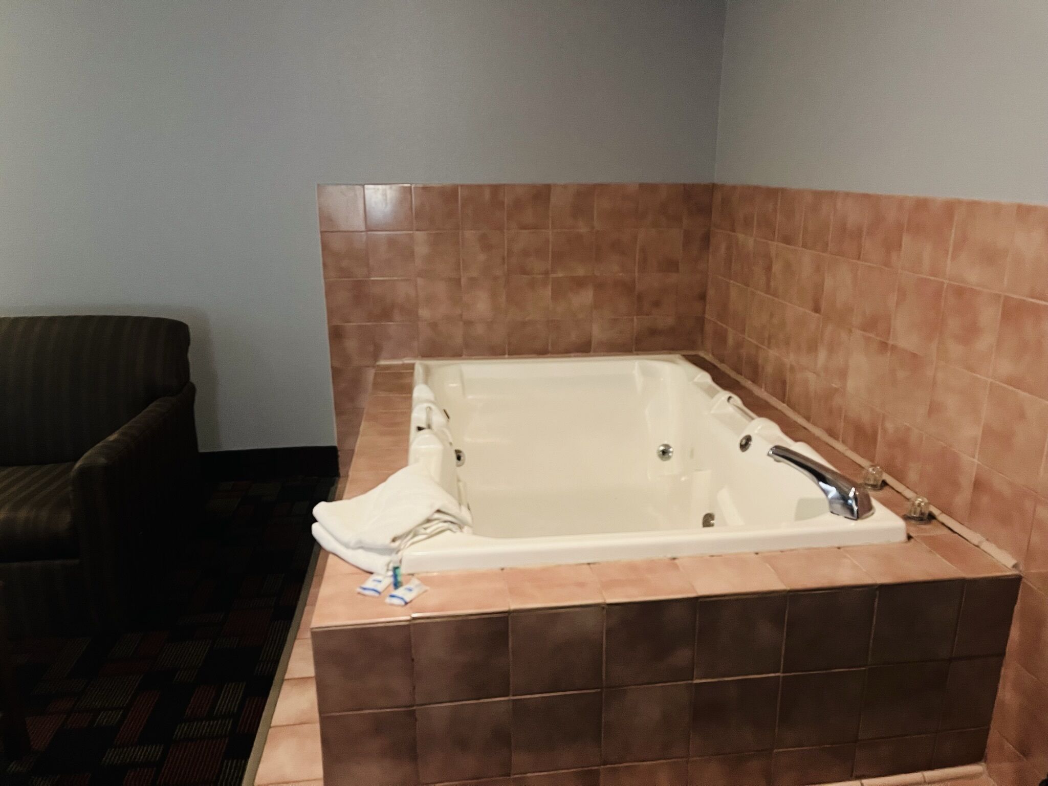 Une salle de bain avec une baignoire, des murs carrelés et un fauteuil de couleur sombre.