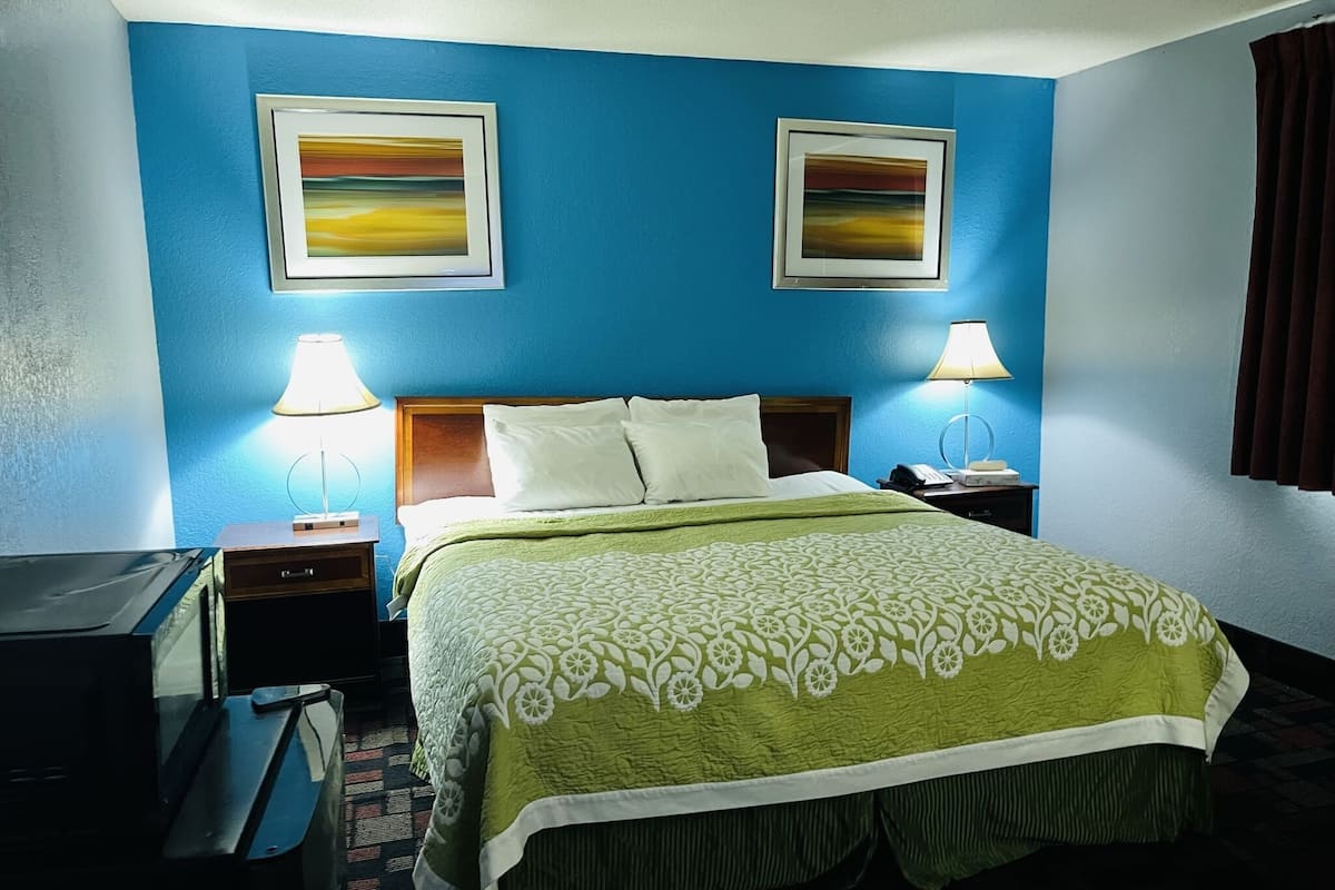 A hotel room with a bed, two bedside lamps, a desk with a printer, and two framed pictures on the wall.