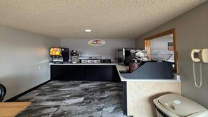 A compact hotel room with a kitchenette, a small dining area, a trash bin, and a phone on the wall.