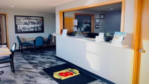 A reception area with a counter, chairs, a framed welcome sign, and a doormat with a logo.