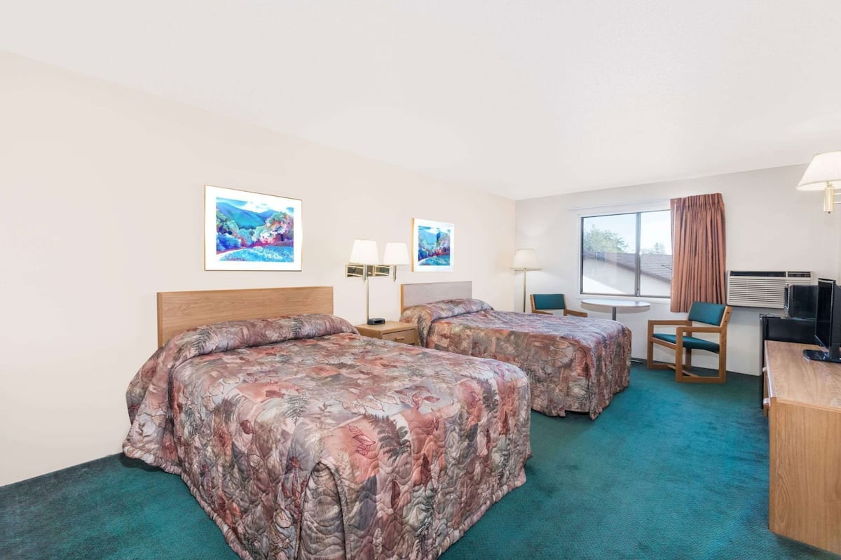Ein Hotelzimmer mit zwei Betten, einem Schreibtisch, einem Sessel, einem Fernseher und Bildern an den Wänden.