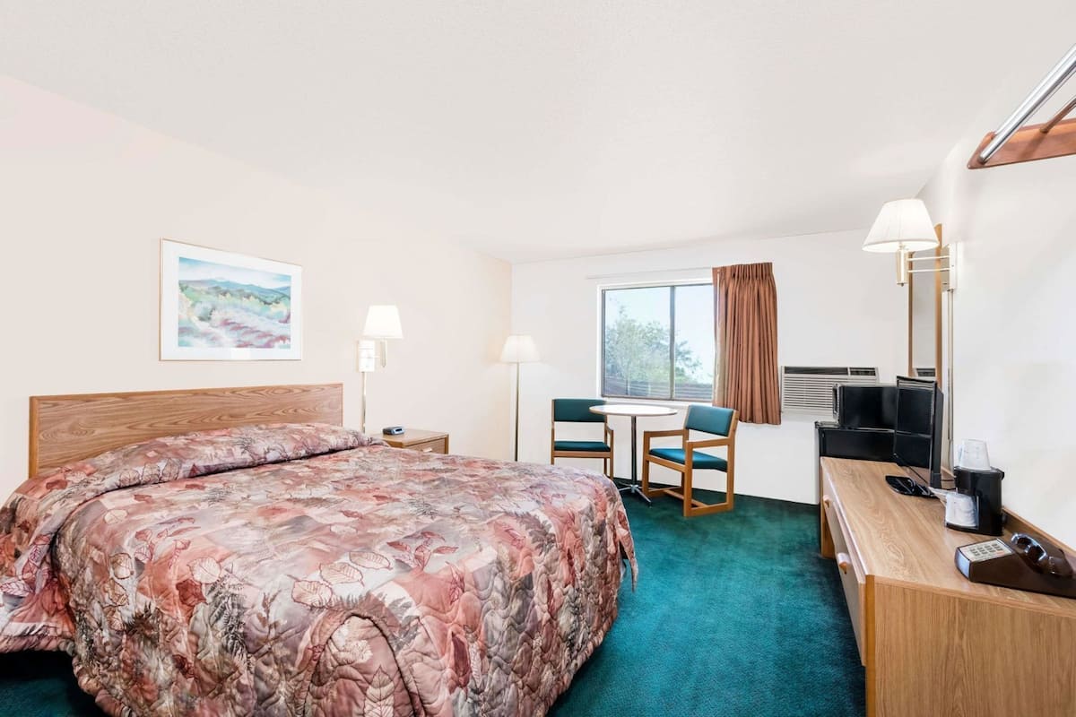 Ein Hotelzimmer mit Bett, Schreibtisch, Stühlen, Fernseher und einem Fenster mit Vorhängen.