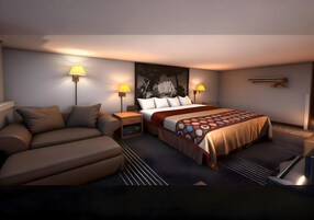 Habitación de hotel moderna con sofá, cama con colcha estampada, dos lámparas de noche y un cuadro abstracto grande en la pared.