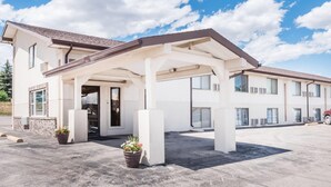 A two-story hotel with a covered entrance, outdoor seating area, and potted plants.