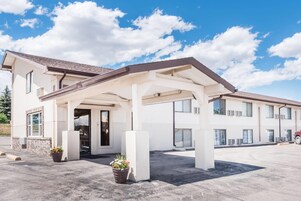 Un hotel de dos pisos con vestíbulo techado, zona de estar exterior y plantas en macetas.