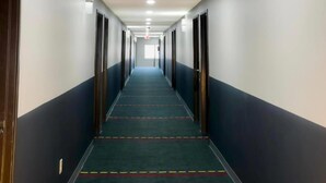 A long, narrow hotel corridor with doors on both sides, a carpeted floor, and a ceiling with recessed lighting.