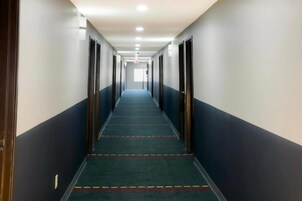 Un largo y estrecho pasillo de hotel con puertas a ambos lados, suelo alfombrado e iluminación empotrada en el techo.