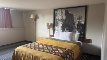 A hotel room with a bed, a nightstand, a lamp, a window with curtains, and a large wall painting.