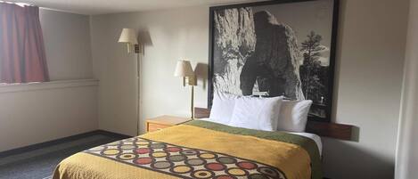 A hotel room with a bed, a nightstand, a lamp, a window with curtains, and a large wall painting.