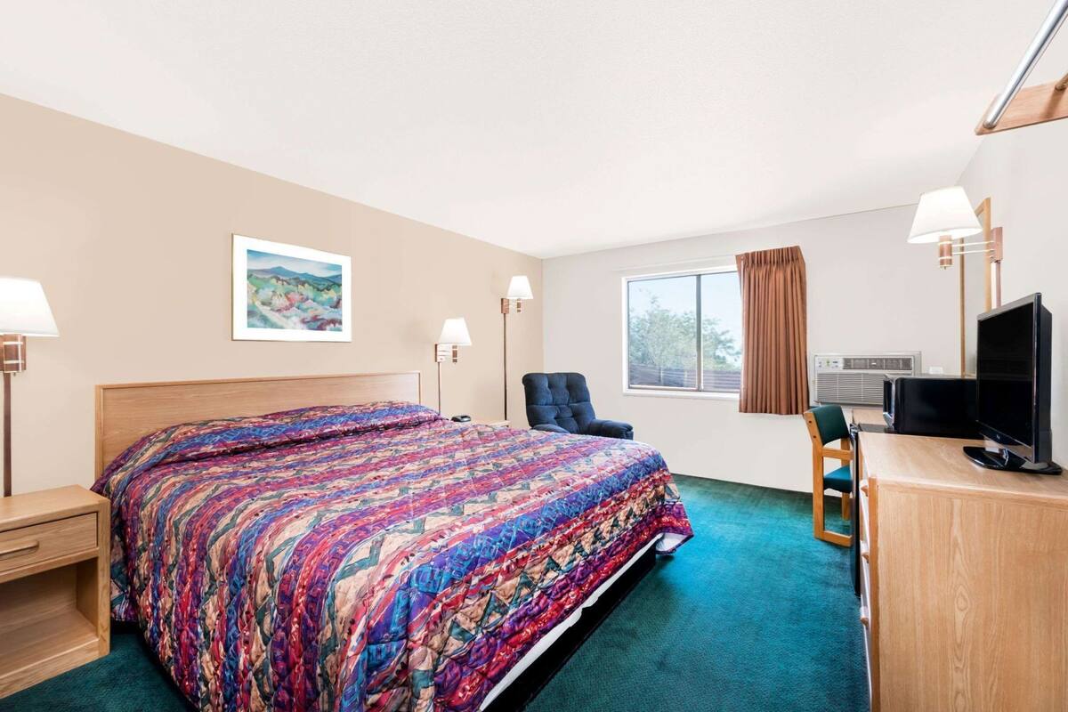 Ein Hotelzimmer mit Bett, Schreibtisch, Stuhl, Fernseher und Fenstern.