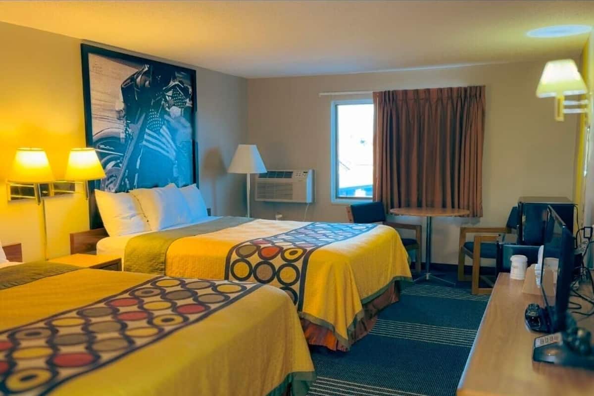 Ein Hotelzimmer mit zwei Betten, einem Schreibtisch, einem Stuhl, einem Computer und einem Fenster mit Vorhängen.
