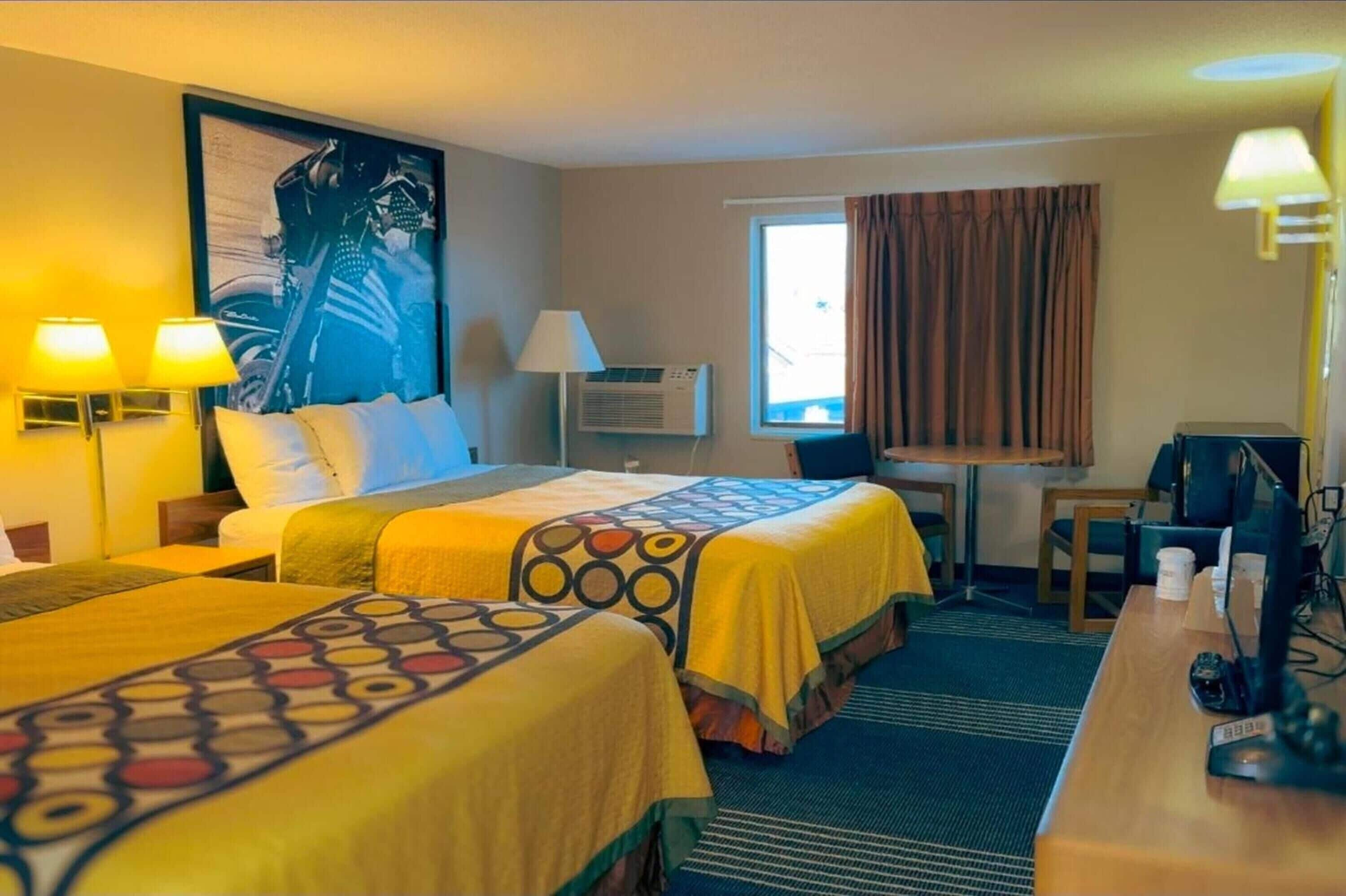 Habitación de hotel con dos camas, un escritorio, una silla, una lámpara, aire acondicionado y una ventana con cortinas.