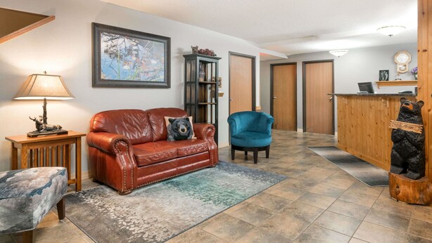 A living room with a leather sofa, a blue armchair, a wooden side table with a lamp, a rug, and a bear statue. - Super 8 by Wyndham Baxter/Brainerd Area (Baxter)