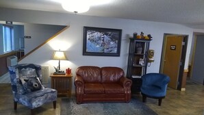 A living room with a brown leather sofa, a blue armchair, and a unique blue armchair with a cloud design. There's a framed picture on the wall, a lamp on a side table, and a rug on the floor. - Super 8 by Wyndham Baxter/Brainerd Area (Baxter)