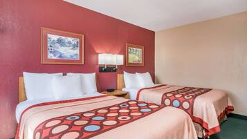 A hotel room with two beds, each with a red and beige bedspread, a nightstand with a lamp, and two framed pictures on the wall.