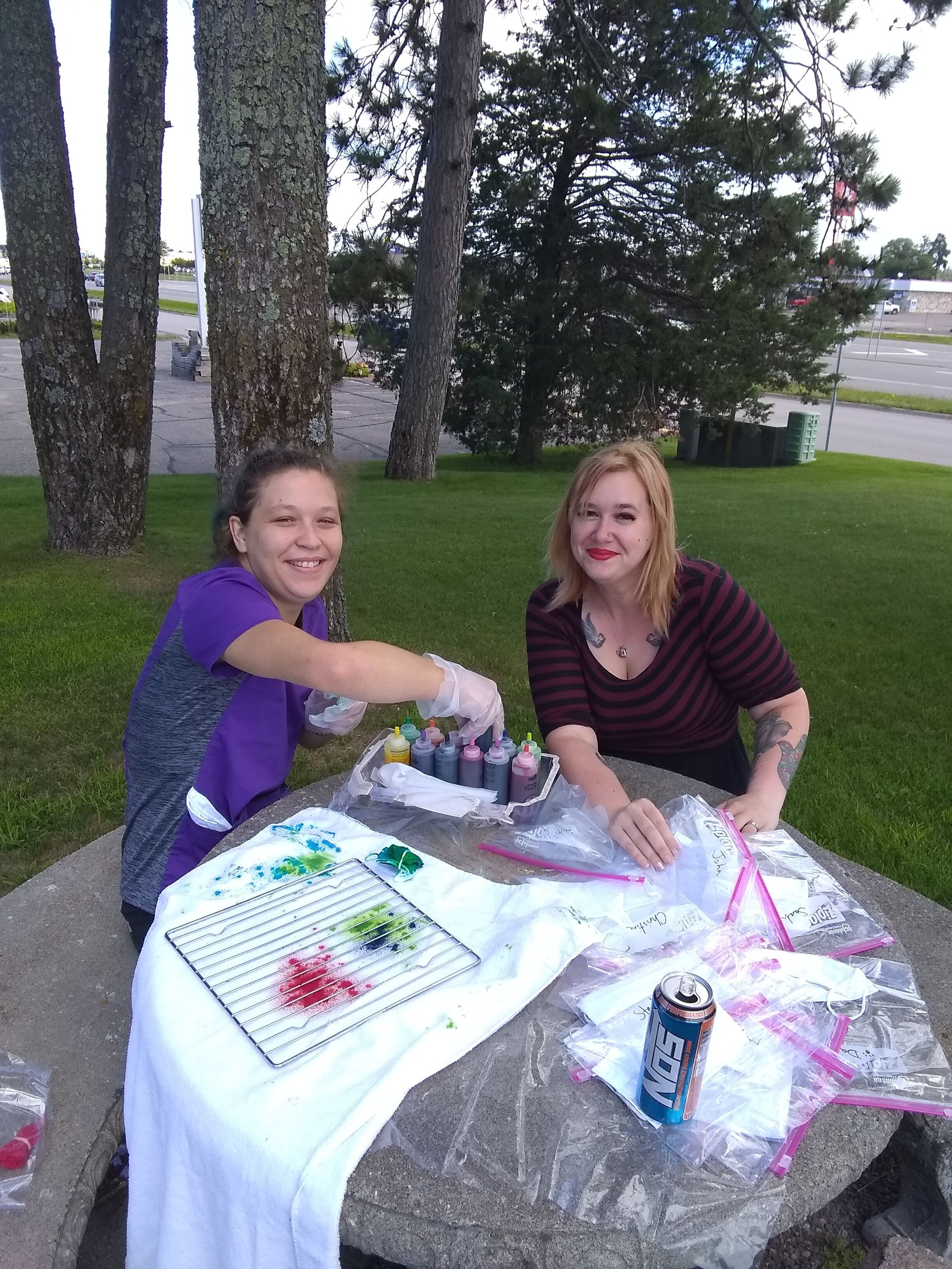 Two people at an outdoor table with art supplies and a can of soda.