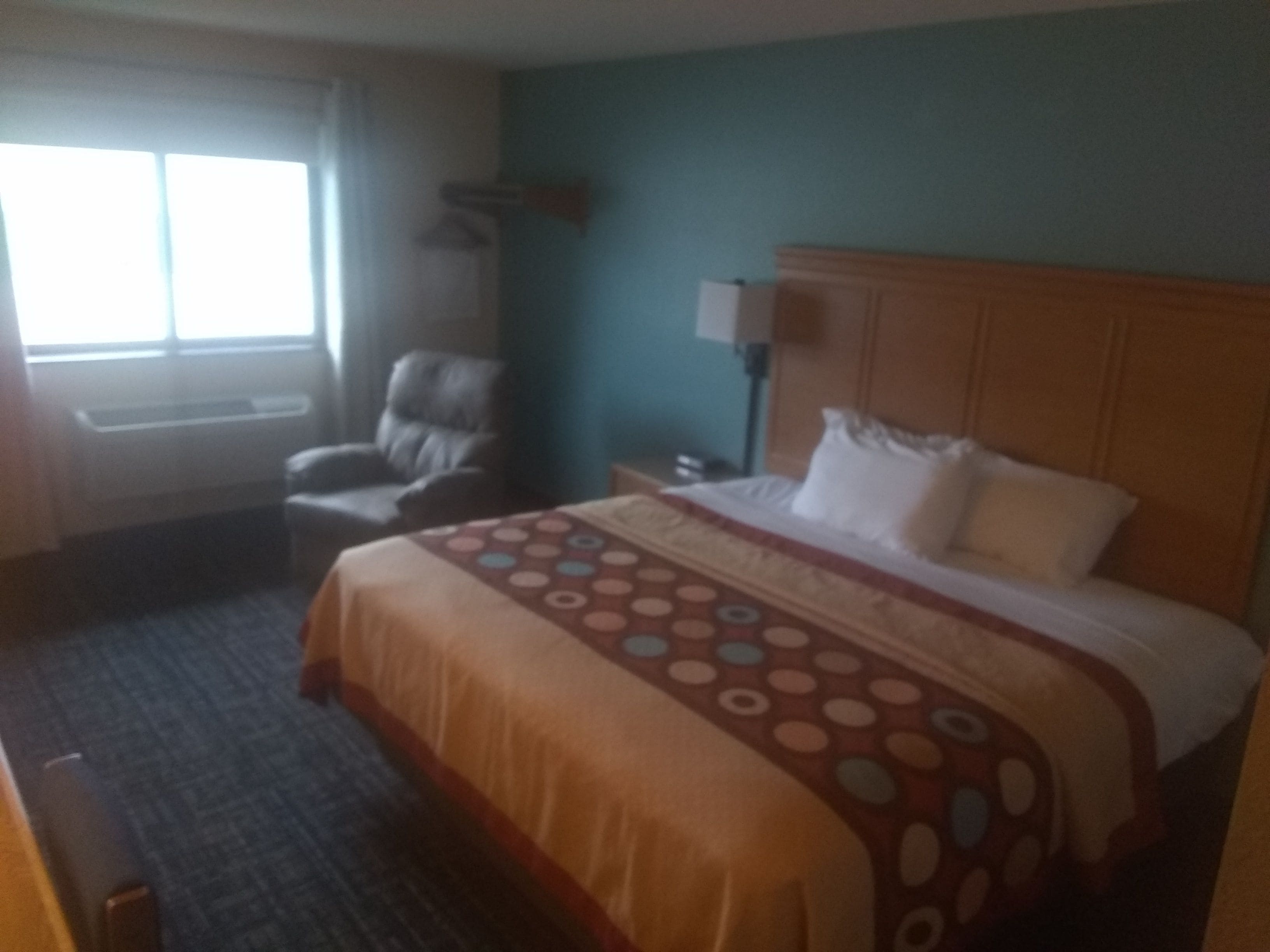 A hotel room with a bed, a chair, a desk, and a window.