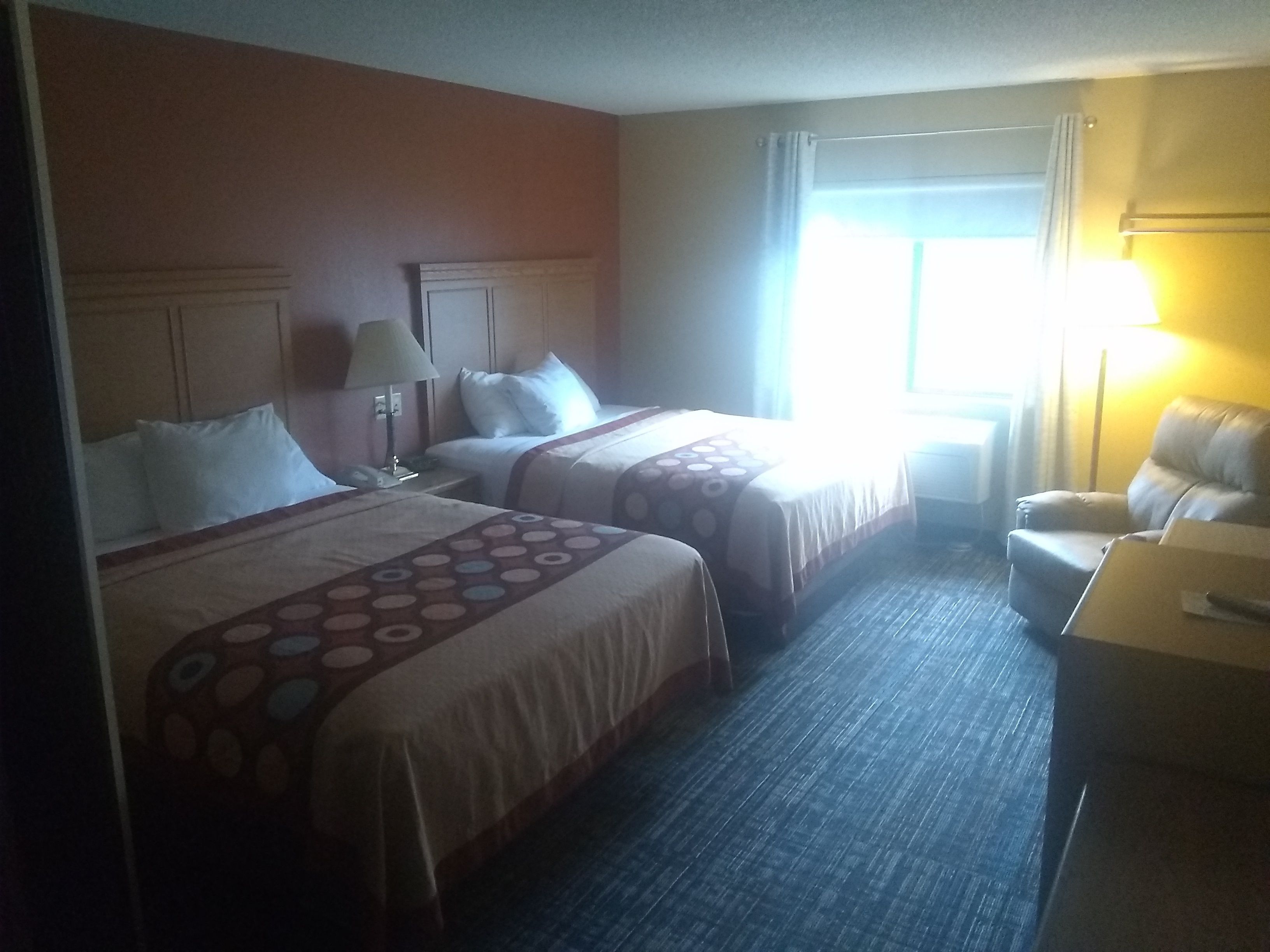 Habitación de hotel con dos camas, un escritorio, una silla y una ventana con cortinas.