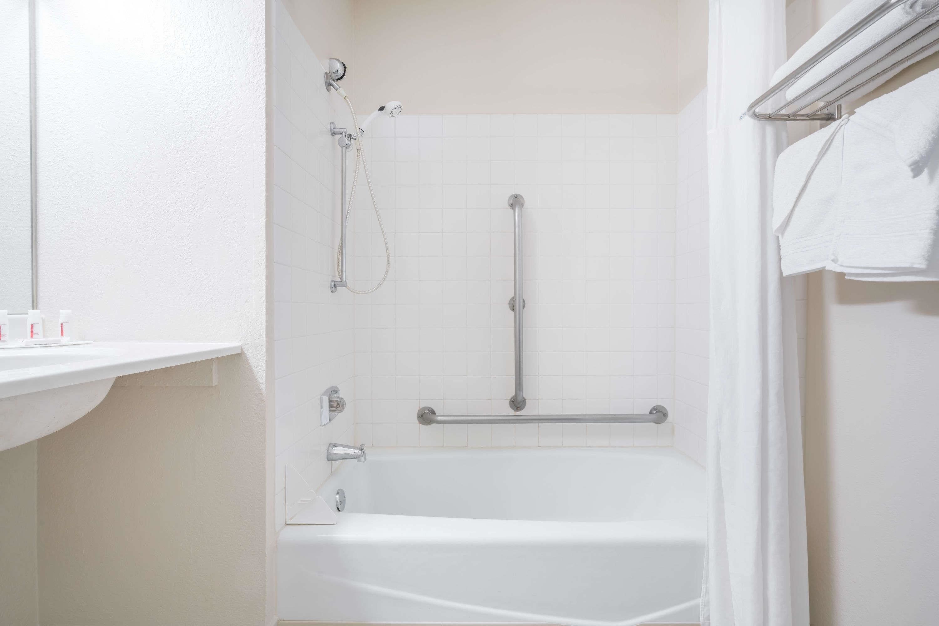 Un baño con una bañera blanca, una ducha con cabezal de ducha manual y un perchero con toallas.