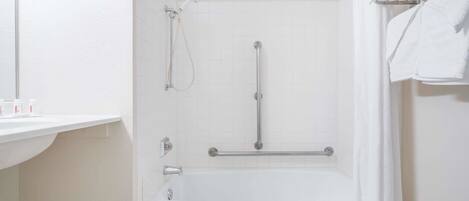 Une salle de bain avec une baignoire blanche, une douche équipée d’un pommeau de douche à main et un porte-serviettes avec des serviettes.