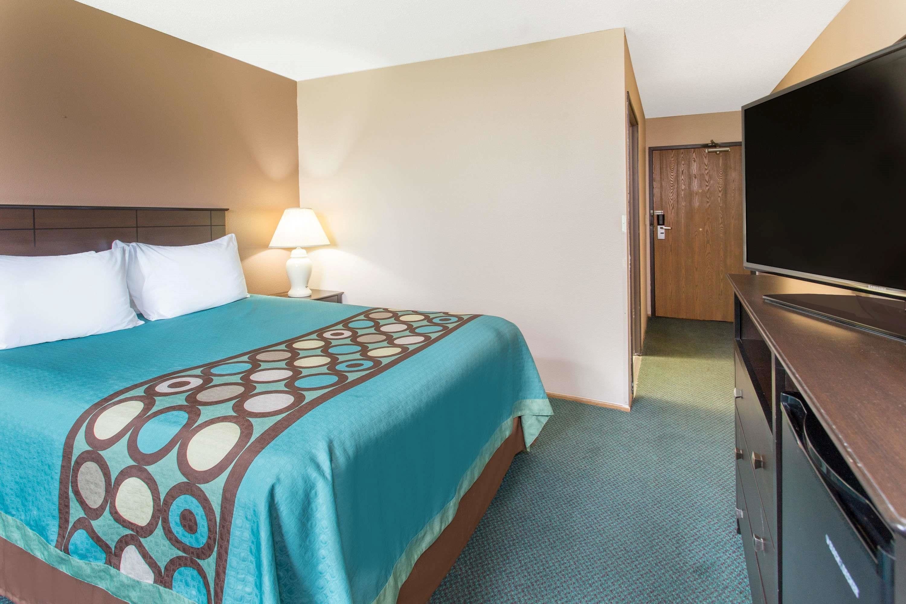 A hotel room with a bed, a TV, a lamp, and a door.