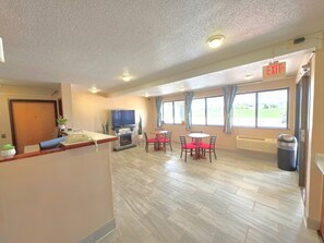 Un hall de hotel con chimenea, televisor, zona de comedor con mesas y sillas, y ventanas amplias.