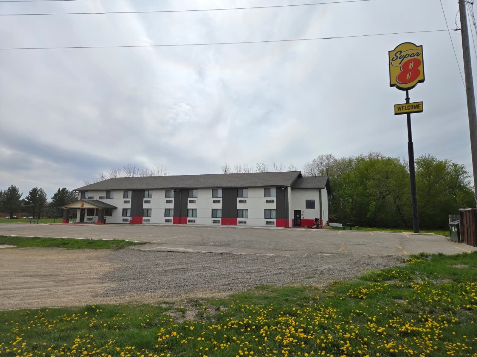 Un motel de la chaîne Super 8, avec un bâtiment à deux étages, un parking et un espace verdoyant agrémenté de fleurs jaunes.