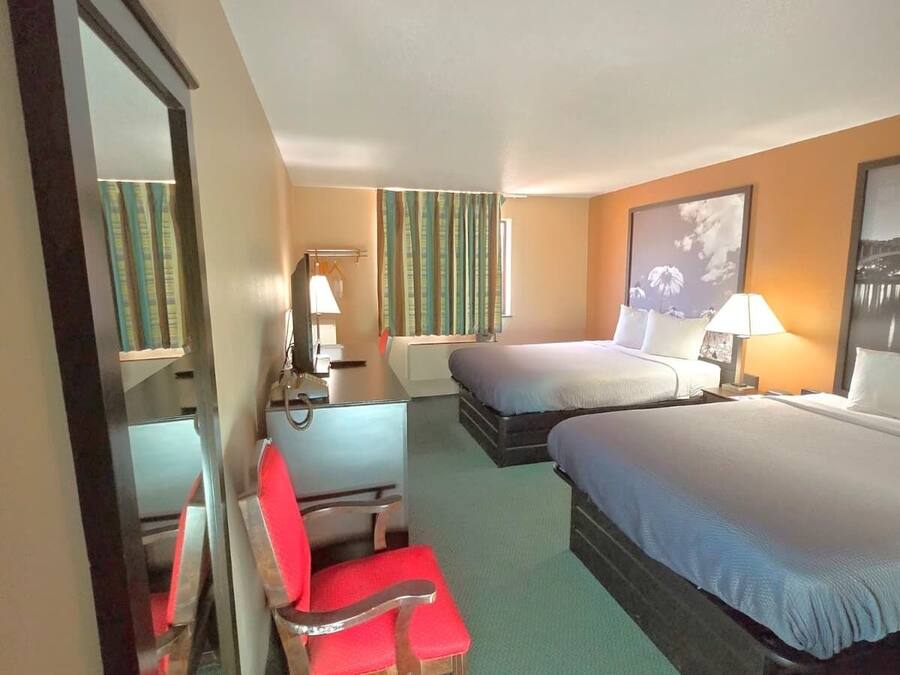 A hotel room with two beds, a desk with a chair, a mirror, and a window with curtains.