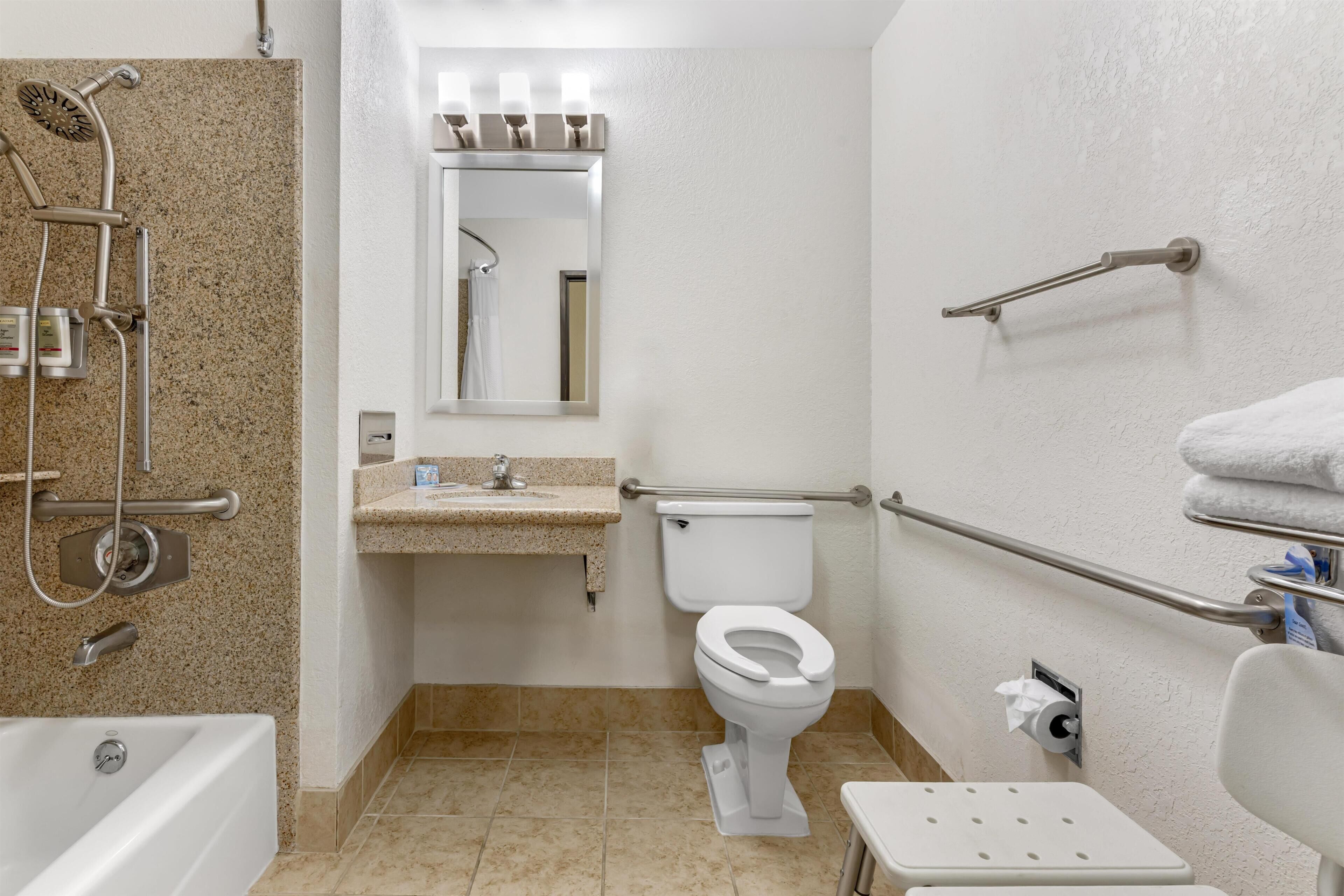 A bathroom with a shower, toilet, sink, and grab bars.
