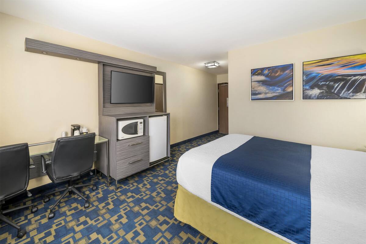 Habitación de hotel con cama, escritorio con computadora, microondas y televisor de pantalla plana montado en la pared.
