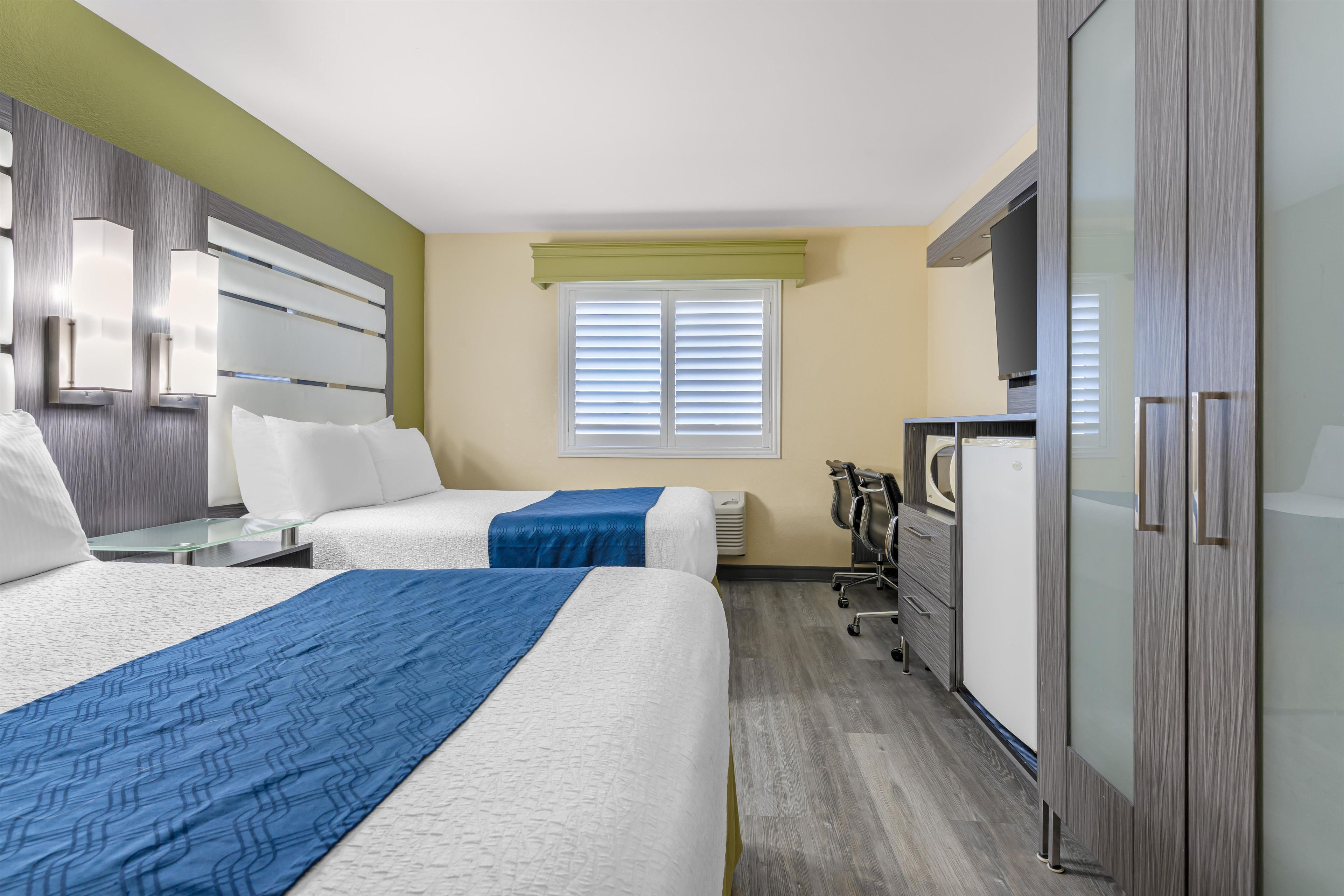 Habitación de hotel con dos camas, un escritorio, un armario y una ventana con persianas.