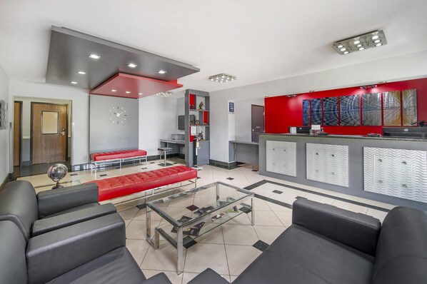 A modern reception area with a red accent wall, a glass coffee table, and a seating area with black sofas. - Best Western Antelope Inn & Suites (Red Bluff)