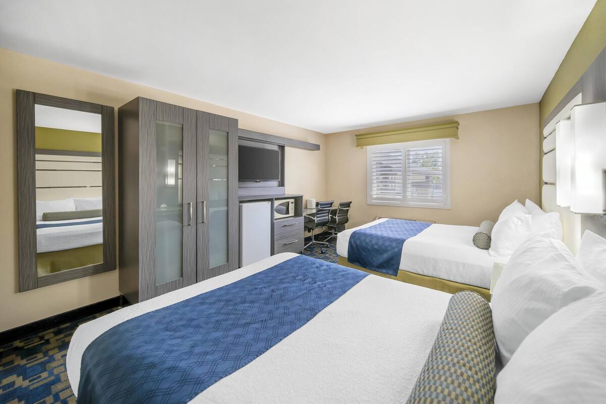 Habitación de hotel con dos camas, un escritorio, un televisor y una ventana con persianas.