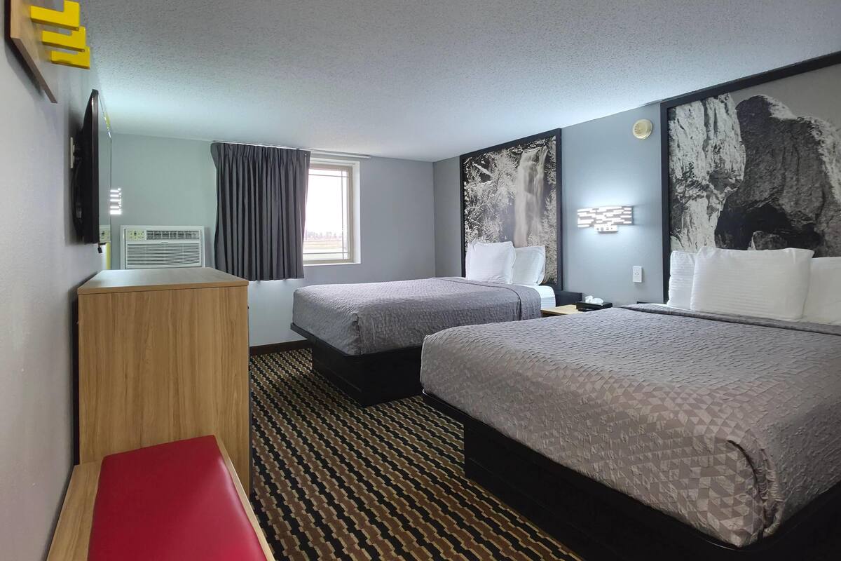 A hotel room with two beds, a desk, a TV, a window with curtains, and artwork on the walls.