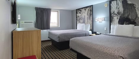 Quarto de hotel com duas camas, uma escrivaninha, televisão, janela com cortinas e obras de arte nas paredes.