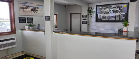 A reception area with a counter, a mounted sign, a wall-mounted picture, a door, and a potted plant.