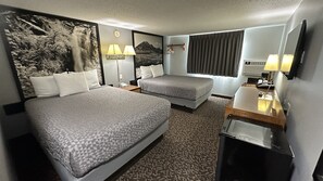 Two single beds with patterned headboards and a desk with a lamp and storage.