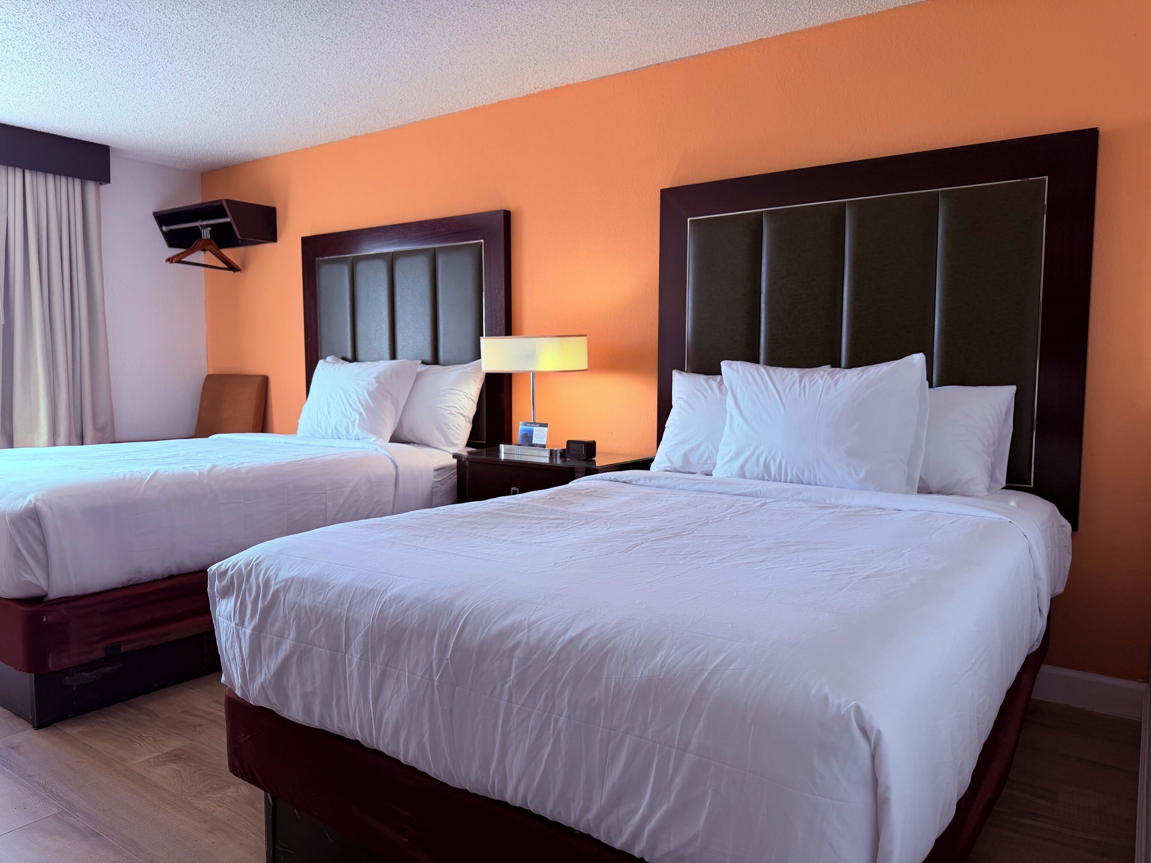 A hotel room with two beds, a nightstand with a lamp, and a wall-mounted TV.
